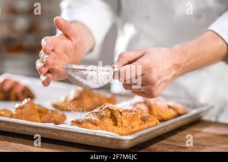 Köche reichen mit einem kleinen Sieb über das Backen Stockfoto