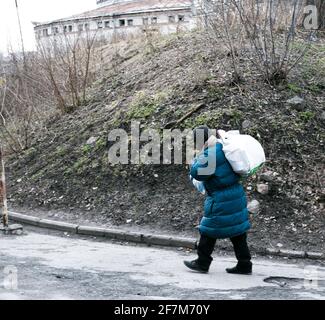 Eine arme, schlecht gekleidete Frau geht die Straße entlang mit einer Tasche auf dem Rücken. Die Frau hat weder Geld noch einen Ort zum Leben. Stockfoto