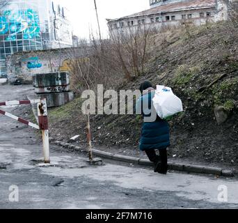 Eine arme, schlecht gekleidete Frau geht die Straße entlang mit einer Tasche auf dem Rücken. Die Frau hat weder Geld noch einen Ort zum Leben. Stockfoto