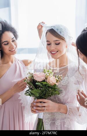 Lächelnde Braut hält Hochzeit Blumenstrauß in der Nähe interracial Brautjungfern Stockfoto