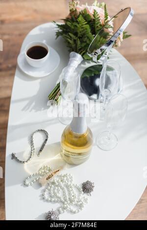 Hochwinkelansicht von Perlenkette, Champagner, Hochzeitsstrauß und Tasse auf dem Couchtisch Stockfoto