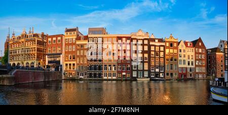 Häuser und Touristenboote auf dem Amsterdamer Grachtenpier Damrak On Sonnenuntergang Stockfoto