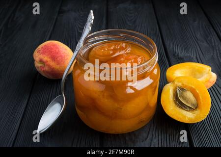 Aprikosenmarmelade und Aprikosen auf dem schwarzen Holzhintergrund.Nahaufnahme. Stockfoto