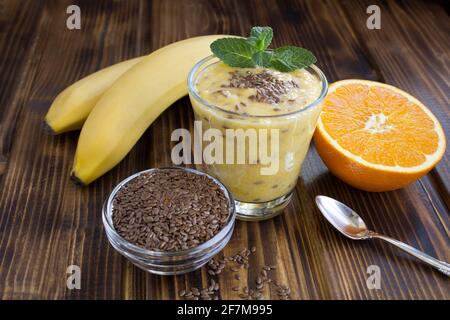Smoothies mit Leinsamen, Orange und Banane im Glas auf dem braunen Holzhintergrund. Nahaufnahme. Stockfoto