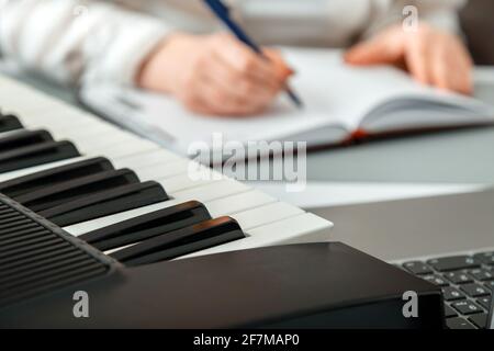 Frau komponiert Musik, weibliche Hände schreiben Notizen oder Lieder in ein Musikbuch. Teen Mädchen lernt, Klaviermusik zu spielen, macht Notizen im Notizbuch. Synthesizer-Klavier Stockfoto