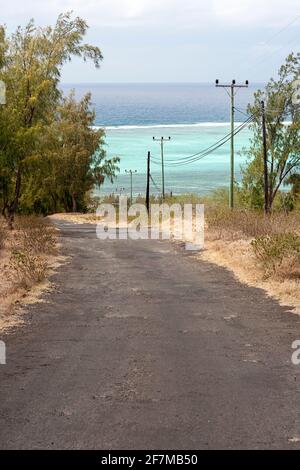 Straße, die von einem Hügel in Richtung einer abgeschiedenen Bucht mit türkisfarbenem Wasser und einem spektakulären Korallenriff führt, Rodrigues Island im Indischen Ozean, Mauritius Stockfoto