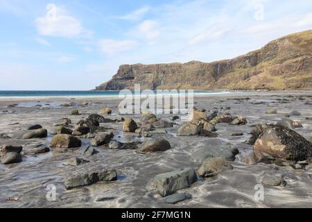 Blick über den Strand mit großen, abgerundeten Felsen, Wellen brechenden Klippen, blauem Himmel mit Wolken, strahlendem Sonnenschein Stockfoto