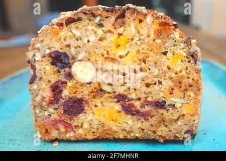 Ein Stück Brot mit getrockneten Früchten auf blauem Teller, getrockneten Aprikosen, Rosinen, Pflaumen und Haselnüssen, Draufsicht. Stockfoto