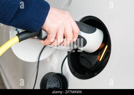 Frau führt das Netzkabel in ein Elektroauto ein Zum Aufladen Stockfoto