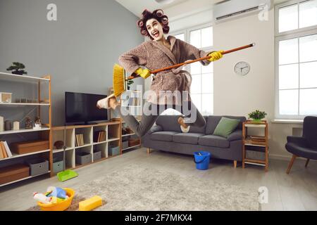 Glücklich energische Hausfrau spielen auf vorgeben Mop Gitarre beim Aufräumen Hoch in ihr Haus Stockfoto