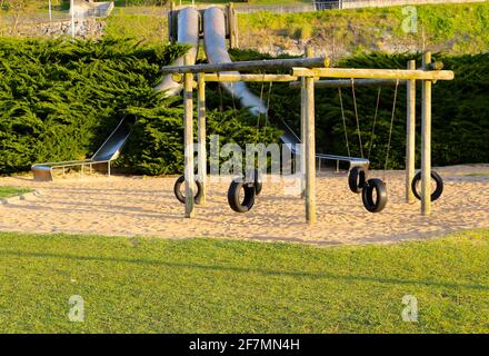 Gummireifen Schaukeln hing an einem Holzrahmen und Metallrohrrutschen mit natürlichem Sandboden Morgen Sonne Santander Cantabria Spanien Stockfoto