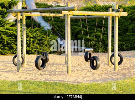 Gummireifen Schaukeln hing an einem Holzrahmen und Metallrohrrutschen mit natürlichem Sandboden Morgen Sonne Santander Cantabria Spanien Stockfoto