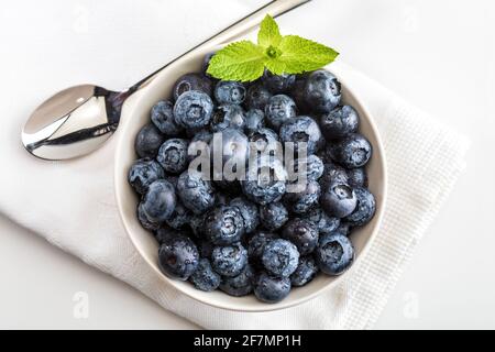 Frische und rohe Heidelbeeren mit Wassertropfen. In Schüssel auf weißer Serviette mit Löffel und fertig zum Essen. Draufsicht mit Kopierbereich. Stockfoto