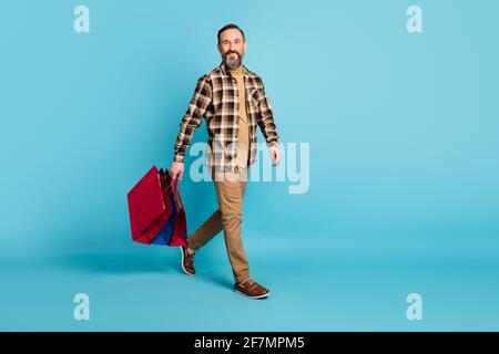 Foto in voller Größe von reifen positiven Mann gehen einkaufen halten Taschen Pakete isoliert auf blauem Hintergrund Stockfoto