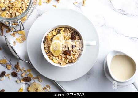 Milchschüssel mit Vollkorngetreide, Frühstücksflocken und Krug Milch. Müsli mit getrockneten Früchten und getrockneten Früchten. Mit Kopierbereich. Auf hellem Hintergrund. Stockfoto