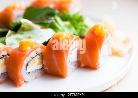 Sushi-Rollen mit Lachs, Avocado und Reis lagen auf weißem Teller, Nahaufnahme Studiofoto mit selektivem Weichfokus Stockfoto