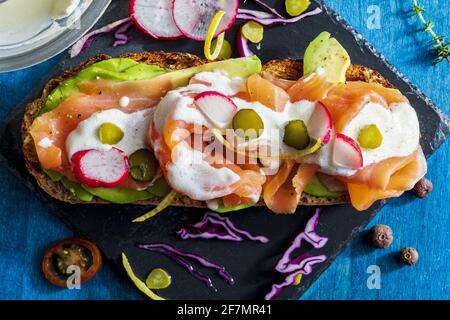 Appetitlich und gesund geräucherter Lachs mit Avocado, Gemüse (Rettich, Zitrone, Rotkohl, Gurke) und Joghurtsauce auf geröstetem Vollkornbrot. Zu Hause Stockfoto