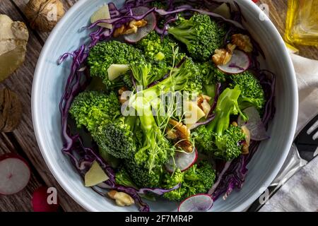 Nahaufnahme des Tellers mit einem gesunden vegetarischen Salat aus gedünstetem Brokkoli, frischen Radieschen, Walnüssen, Rotkohl, Ingwer und nativem Olivenöl extra. Medite Stockfoto