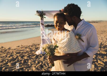 Glückliches afroamerikanisches Paar in der Liebe heiraten, umarmen am Strand während des Sonnenuntergangs Stockfoto