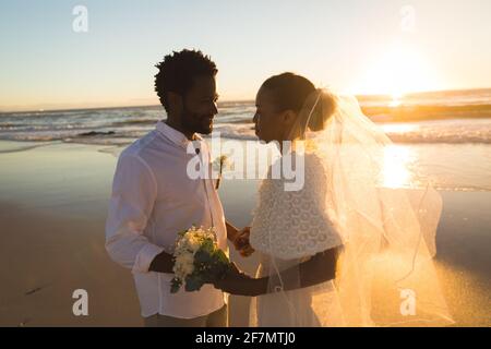 Glückliches afroamerikanisches Paar in der Liebe heiraten, Hände am Strand während des Sonnenuntergangs halten Stockfoto