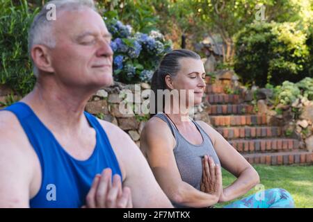 Glückliches kaukasisches Seniorenpaar im Garten, das Yoga praktiziert, sitzt und meditiert Stockfoto