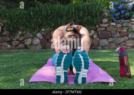 Kaukasische ältere Frau, die im Garten trainiert, auf einer Yogamatte sitzt, die sich dehnt Stockfoto