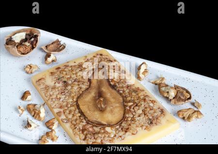 Dessert-Käse mit Birnen und gehackten Walnüssen, auf einem Schneidebrett. Selektiver Fokus, schwarzer Hintergrund Stockfoto