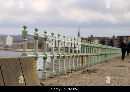 Alter grüner und rostiger Metallzaun zwischen dem Gehweg und Die Küste entlang der Portobello Beach Promenade in Edinburgh Stockfoto