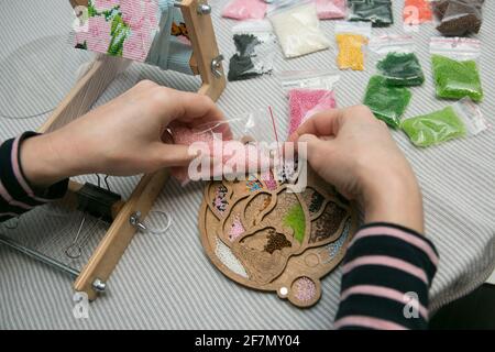 Weben aus Perlen. Nahaufnahme - die Hände einer Frau ziehen Perlen an einen Faden und machen Schmuck. Die Frau webt gern aus Perlen. Stockfoto