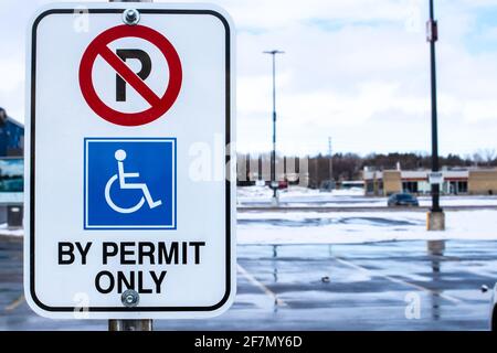 Kein Parken, nur mit Genehmigung Schild mit dem internationalen Zugangssymbol auf einem rechteckigen vertikalen Schild auf einem schmutzigen und verschneiten Parkplatz. Stockfoto