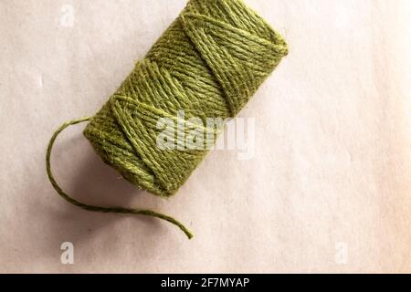 Ein Zylinder aus olivgrünem Garn mit einem einzelnen Strang, der bei natürlichem Licht auf einem Pergamentpapierhintergrund locker hängt, Ontario, Kanada, 2021. Stockfoto