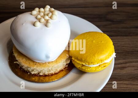 Herzförmiger Vanille-Passionfrucht-Kuchen auf einem Goldfolienkreis, Februar 2021. Mango und Passionfrucht Creme gefüllte Französisch Macaron auf der Seite eines weißen Stockfoto