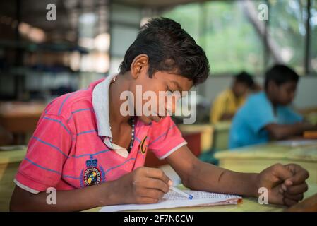 Varanasi, Indien. 10-14-2019. Ein männlicher Jugendlicher, der in seinem Lehrbuch an einem Internat schreibt, während er seine Hausaufgaben macht. Stockfoto