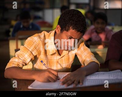 Varanasi, Indien. 10-14-2019. Ein männlicher Jugendlicher mit Brille schreibt in der Schule in sein Lehrbuch, während er seine Hausaufgaben macht. Stockfoto