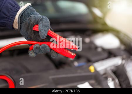 Person, die das rote Jumperkabel neben dem Auto in der Nähe hält Nach oben Stockfoto