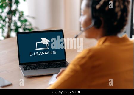 E-Learning-Konzept. Über die Schulter des afroamerikanischen Mädchens auf dem Laptop-Bildschirm. Studentin mit sitzt zu Hause am Schreibtisch und studiert fernab. Online-Schulungen, Webinar, Vortrag Stockfoto