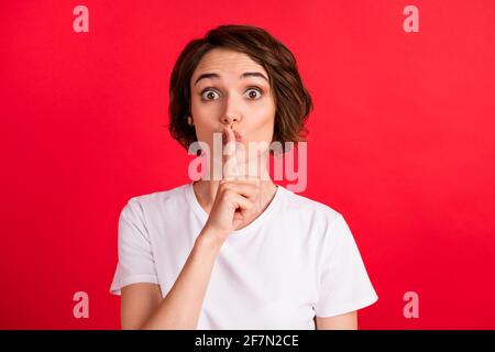 Portrait von attraktiven erstaunt neugierig Mädchen zeigt shh Zeichen oops Isoliert auf einem leuchtend roten Hintergrund Stockfoto