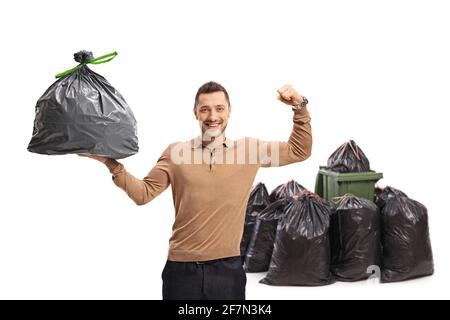 Junger Mann, der einen Müllbeutel in der Hand hält und seinen Bizeps beugt Vor einem Mülleimer isoliert auf weißem Hintergrund Stockfoto