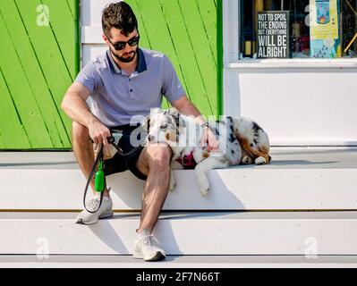 Ein Mann sitzt mit seinem australischen Schäferhund vor dem Social Chair, einem Boutique- und Souvenirladen, am 3. April 2021 in Bay Saint Louis, Mississippi. Stockfoto