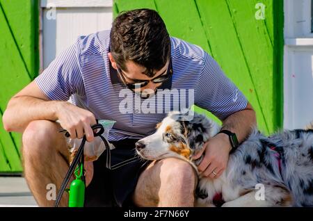 Ein Mann sitzt mit seinem australischen Schäferhund vor dem Social Chair, einem Boutique- und Souvenirladen, am 3. April 2021 in Bay Saint Louis, Mississippi. Stockfoto