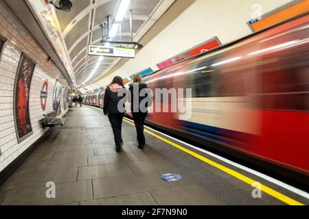 Die Passagiere gehen am Bahnsteig entlang zum Ausgang der Londoner U-Bahnstation Notting Hill Gate, während ein Zug unscharf abfährt. Stockfoto