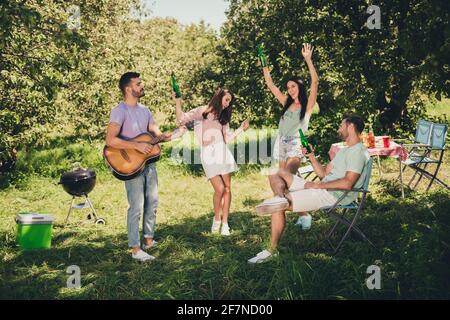 Foto in voller Größe von vier fröhlichen Lächeln Freunde feiern Wochenende Tanz, Gitarre, Bier im Freien im Park Stockfoto