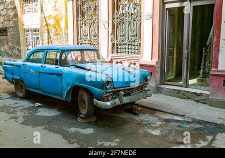 Ein heruntergekommenes, hellblaues amerikanisches Auto aus den 50er Jahren mit dem Vorderrad, das auf einer Radkappe vor Wohngebäuden in der Altstadt von Havanna, Kuba, angehoben wurde. Stockfoto