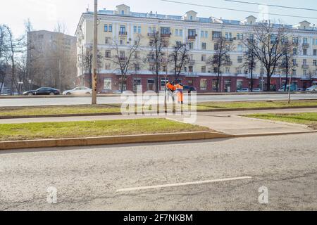 Moskau. Russland. 06. April 2021. Orangefarbene uniformierte Hausmeister, die auf einer Straße in der Stadt den Rasen fegen. Sonniger Frühlingstag. Die Arbeit der Gemeinde Stockfoto