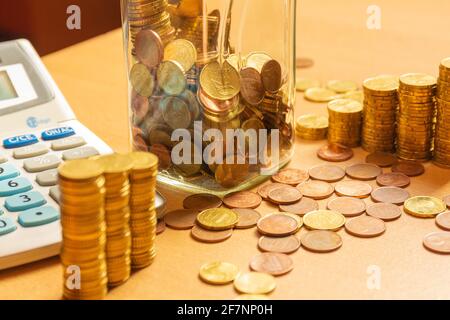 Stapel von Münzen auf einem Tisch mit vielen verschiedenen Münzen um ihn herum und einem Rechner auf einem Holztisch. Sparen Sie Geld Konzept Banner Stockfoto