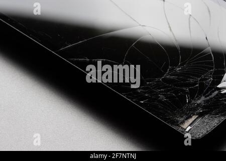 Nahaufnahme eines defekten Smartphones mit gesprungenem Bildschirm auf grauem Hintergrund isoliert. Stockfoto