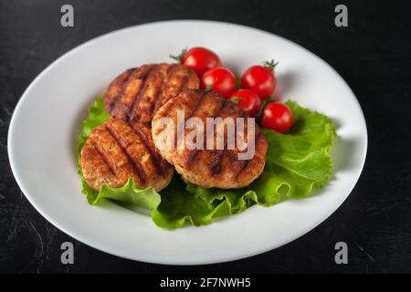 Gebratenes Schnitzel mit Salat und Tomaten auf einem weißen Teller Auf schwarzem Hintergrund Stockfoto