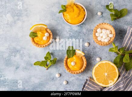 Minitörtchen mit Zitronenquark, Mini-Baiser, Zitronenscheiben und Minze auf blauem Betongrund. Draufsicht. Selektiver Fokus. Stockfoto