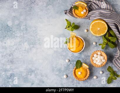 Minitörtchen mit Zitronenquark, Mini-Baiser, Zitronenscheiben und Minze auf blauem Betongrund. Draufsicht. Selektiver Fokus. Stockfoto