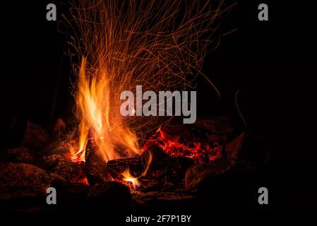 Nachtlager mit verfügbarem Platz. Großes Lagerfeuer vor schwarzem Hintergrund. Funken von Lagerfeuer und Feuer aus der Nähe Stockfoto